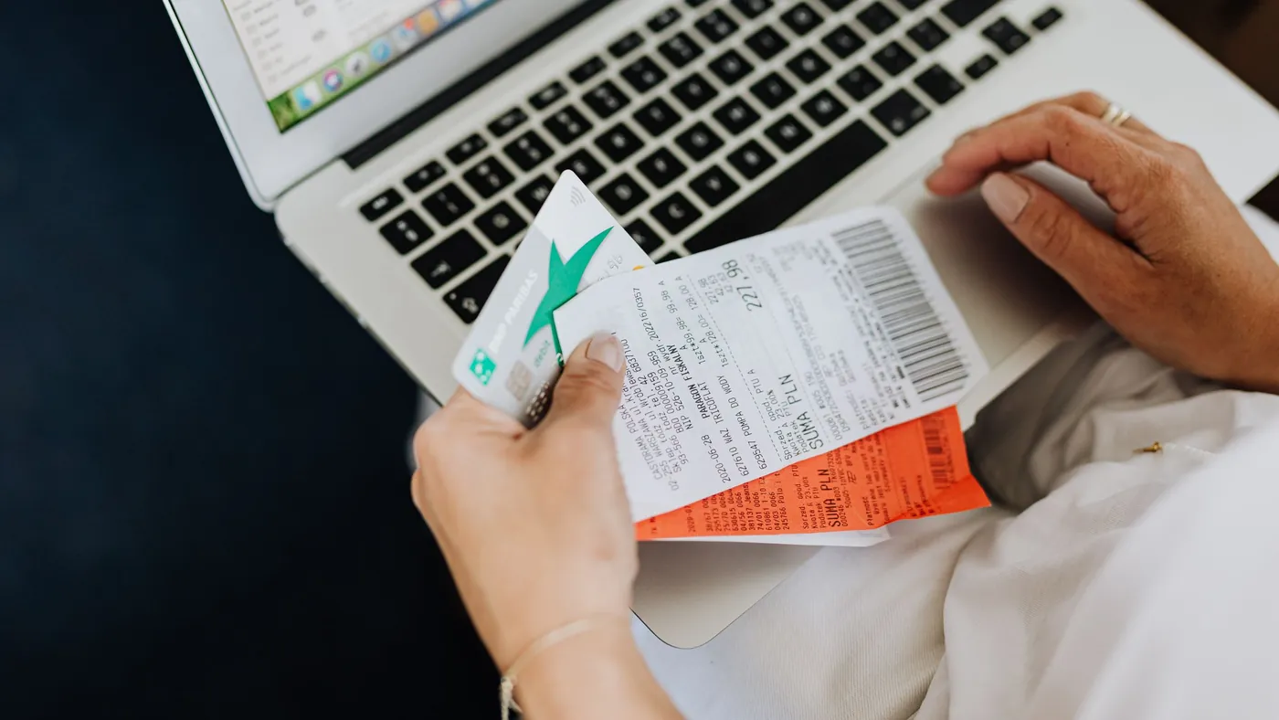 A person holds a bank card and paper receipts over an open laptop keyboard