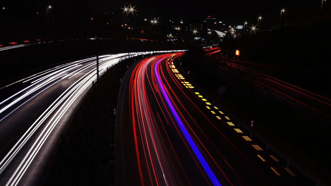 Long exposure photograph of red and white light trails on a multi-lane highway at night