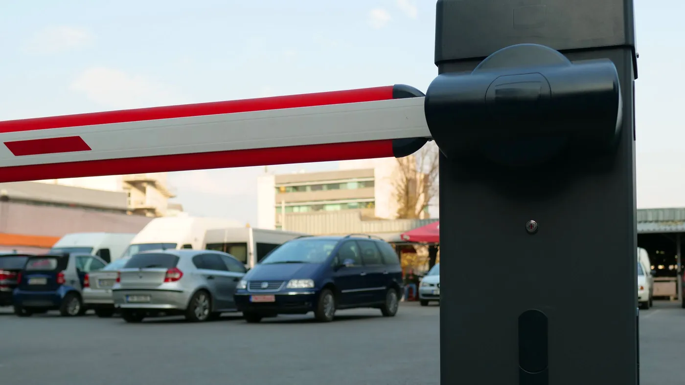An automated parking barrier arm lowered across a vehicle lane with cars waiting behind it