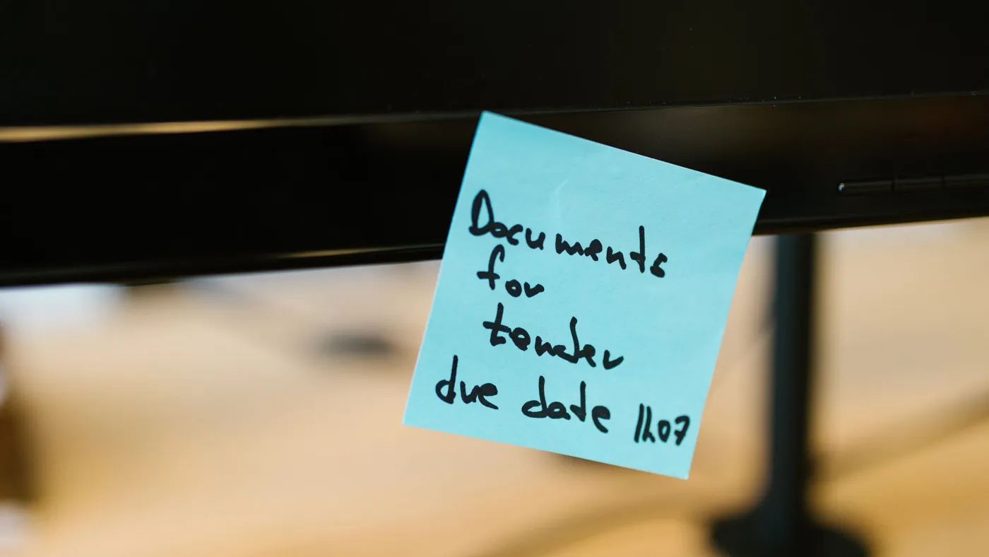 A blue sticky note with a handwritten reminder stuck to the edge of a computer monitor
