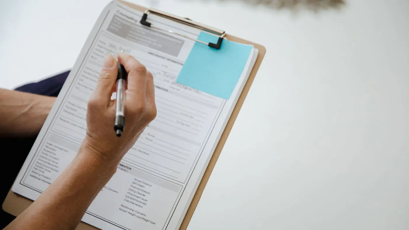 A person writing on a document attached to a clipboard