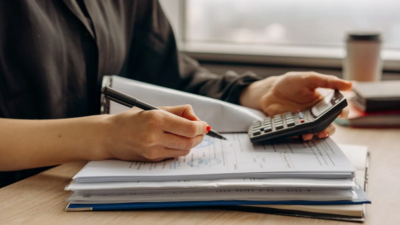 Close-up of a person using a calculator alongside financial documents