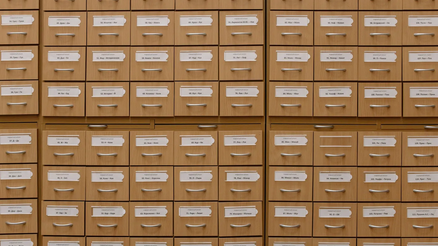 A wall of wooden card catalogue drawers, each with a typed alphabetical label
