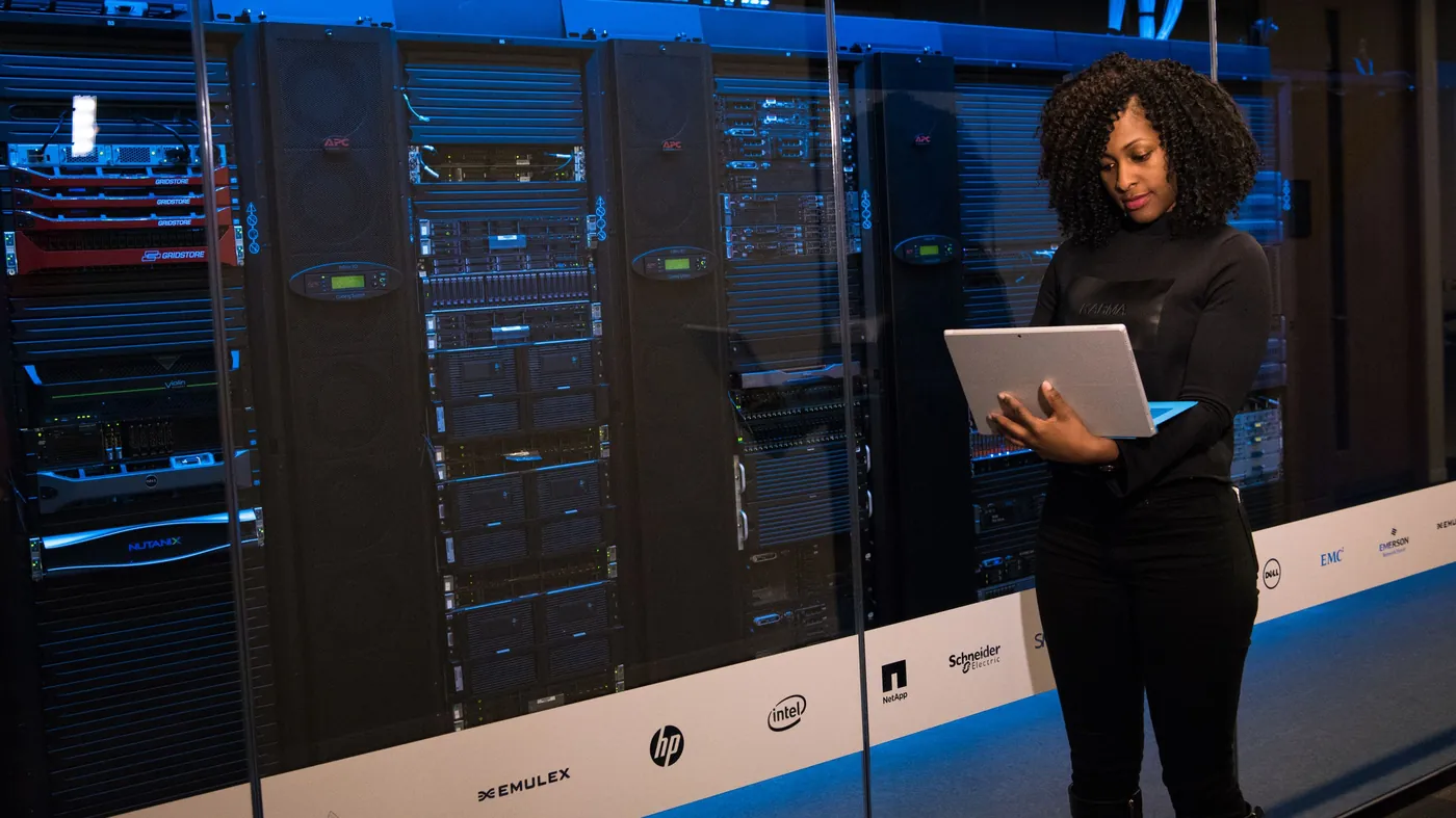 An engineer working on a laptop beside racks of servers in a data centre